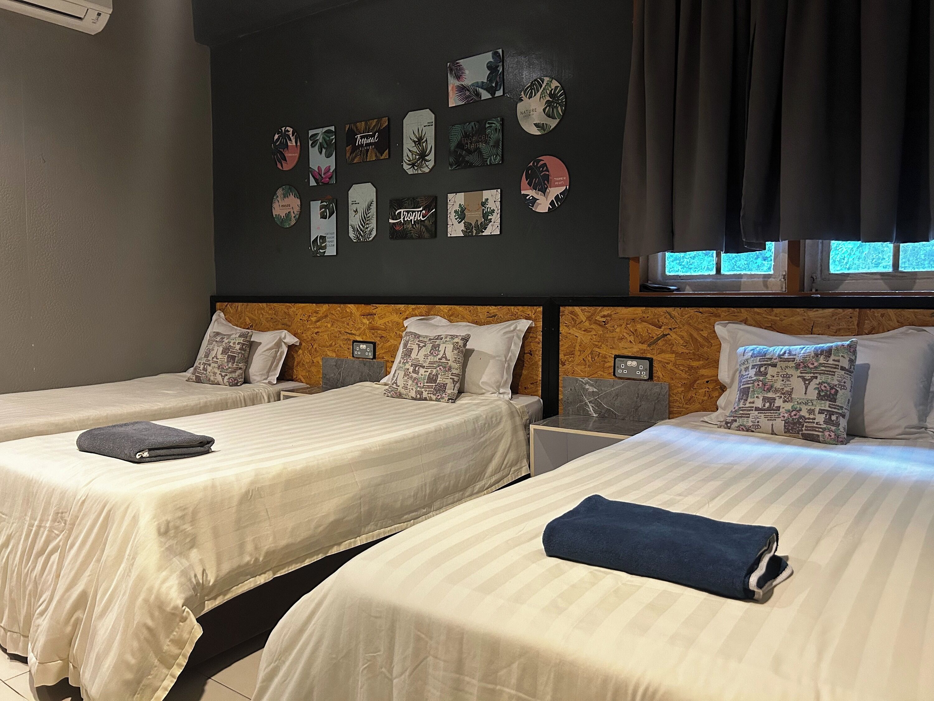 A hotel room with two beds, a wooden headboard, a wall decorated with tropical-themed artwork, and a window with curtains.