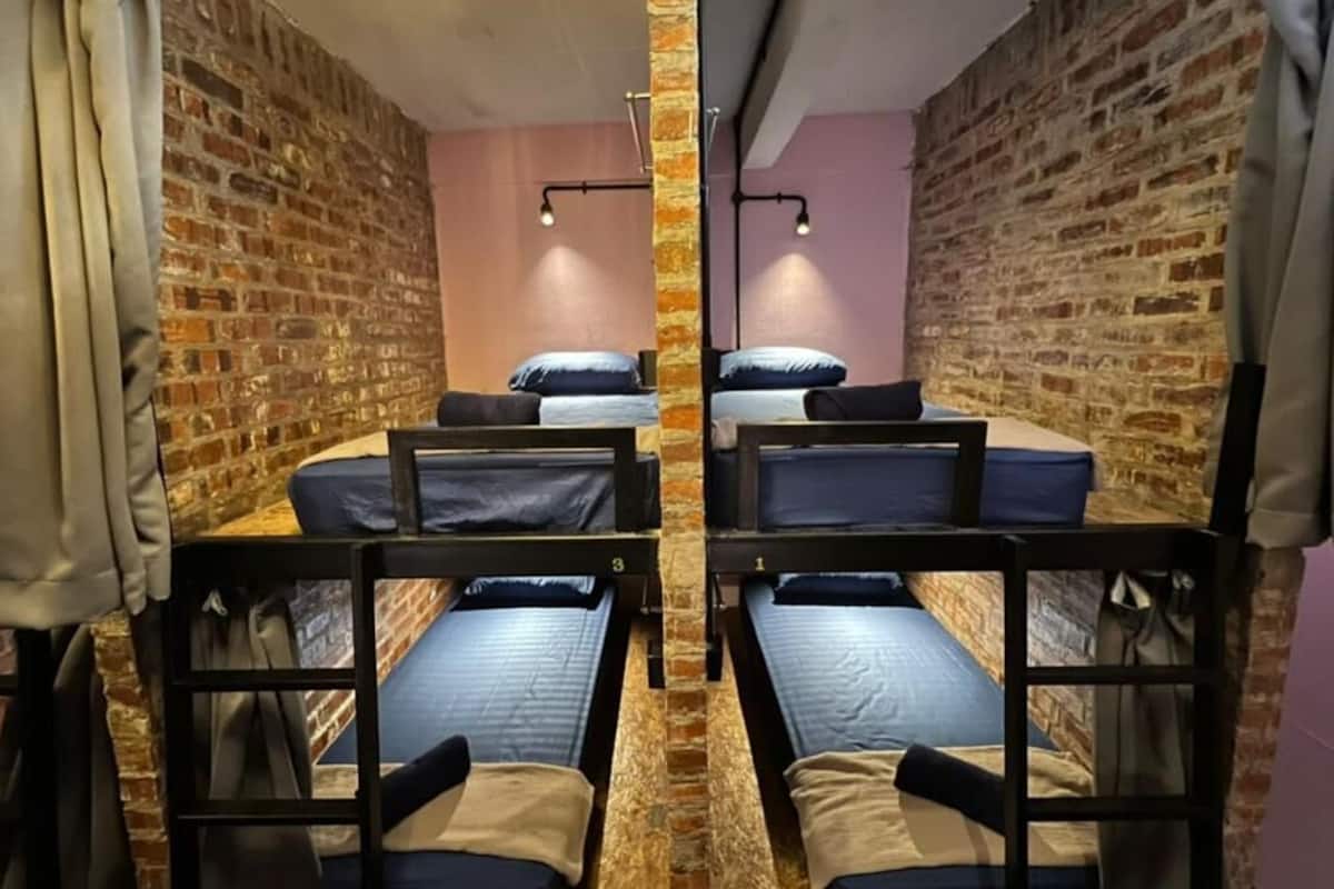 A dormitory room with four bunk beds, brick walls, and a pink accent wall.