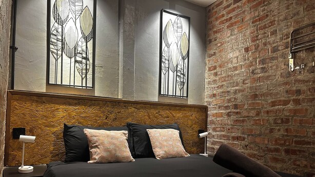 A modern bedroom with a brick wall, a wooden headboard, and two windows with metal leaf designs. - Riverbank Dungun Guesthouse & Cafe (Dungun)