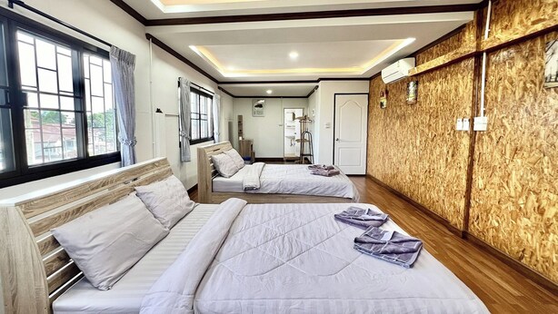 Habitación de hotel con dos camas, cabeceros de madera, un ventanal grande con cortinas, una pared decorativa de madera y un techo con iluminación empotrada.