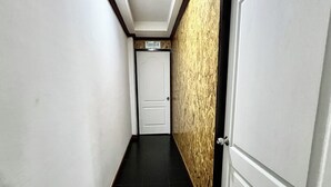 Un pasillo estrecho con una puerta blanca al final, piso de baldosas negras y una pared texturizada a un lado.