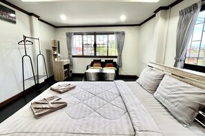 A hotel room with a large bed, two smaller beds, a wardrobe, a mirror, a table with a chair, and a window with curtains. - Good Sleep Guest House (Chiang Mai)