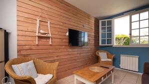 Een kamer met een houten wand, een televisie, rieten meubels, een raam met uitzicht en een radiator.