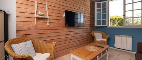 A room with a wooden wall, a television, wicker furniture, a window with a view, and a radiator.