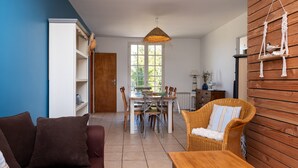Een woonkamer met een bank, een eettafel met stoelen, een rieten fauteuil en een houten wand.