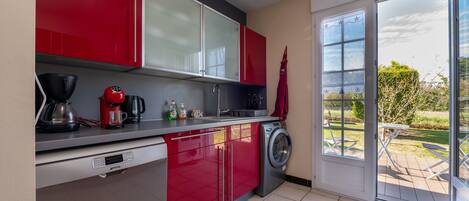 A kitchen with red cabinets, a washing machine, and a coffee maker.