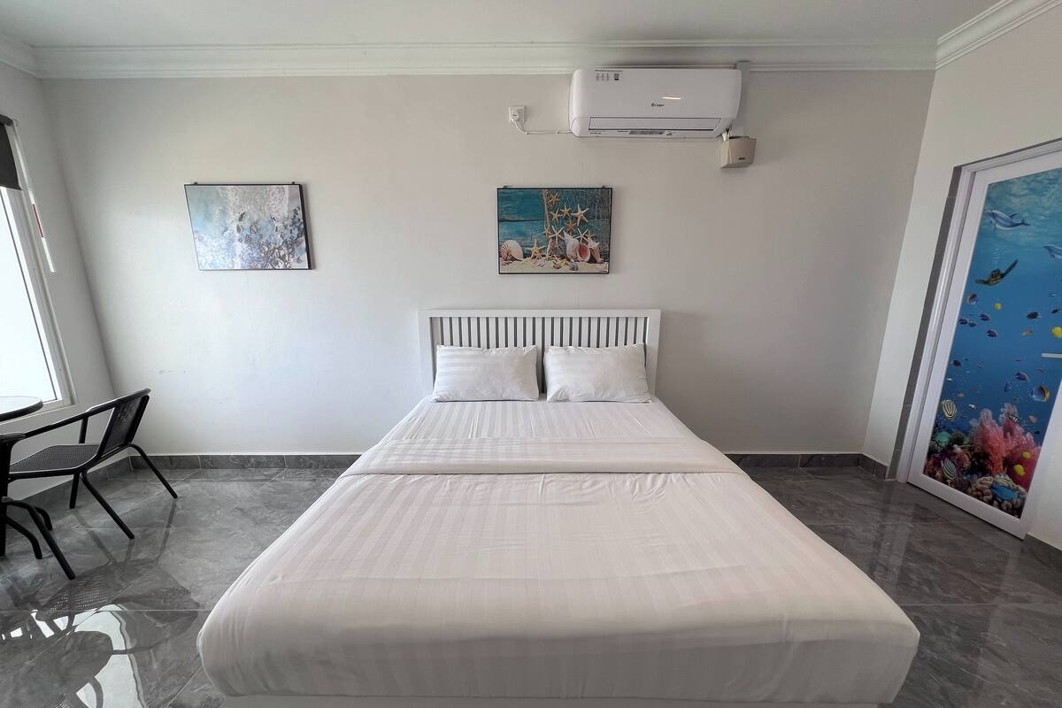 Habitación de hotel con cama, una silla, aire acondicionado y dos cuadros en la pared.