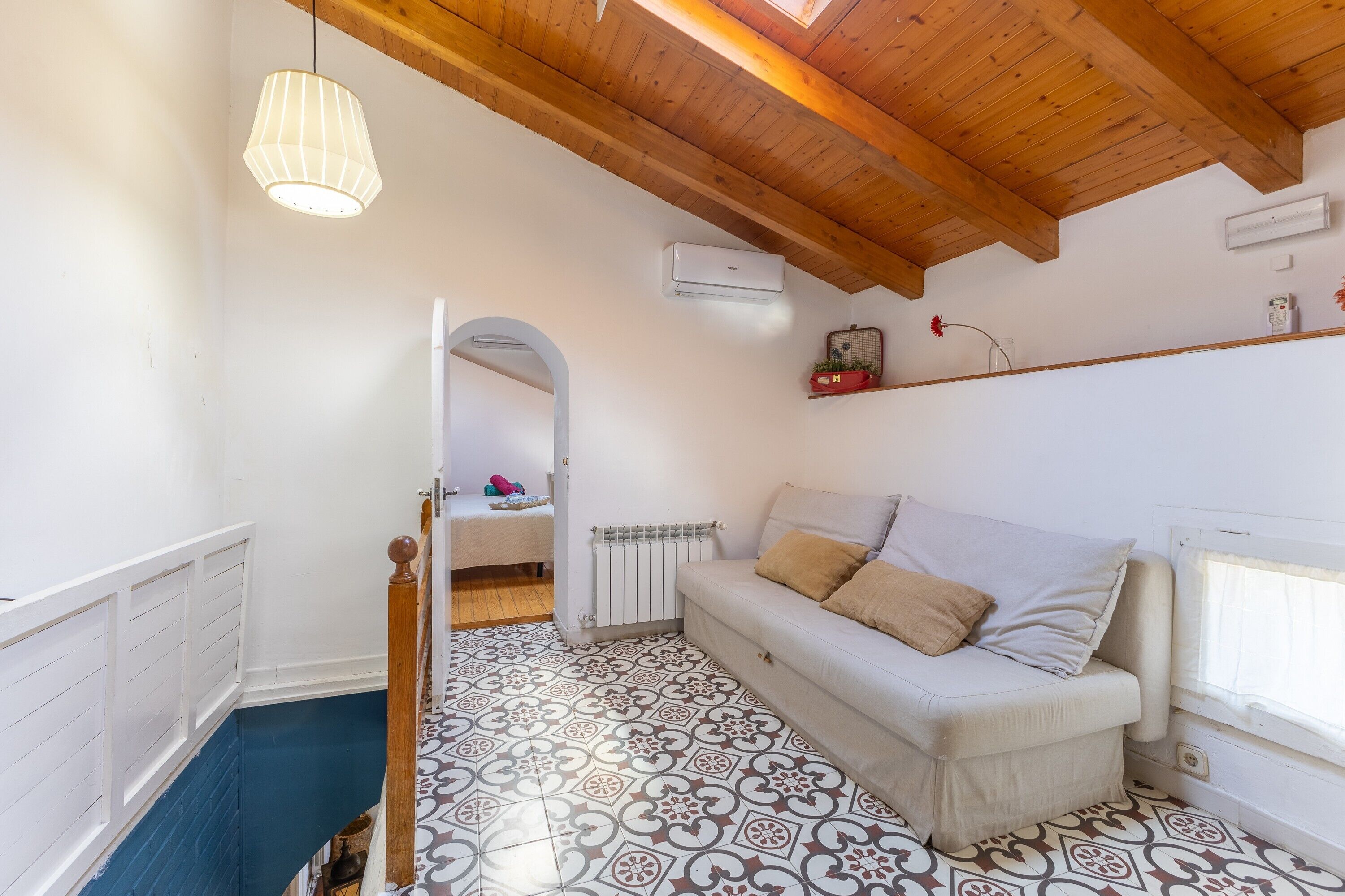 A room with a patterned floor, a white sofa with cushions, a wooden ceiling, and a hanging light fixture.