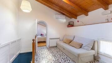 A room with a patterned floor, a white sofa with cushions, a wooden ceiling, and a hanging light fixture.