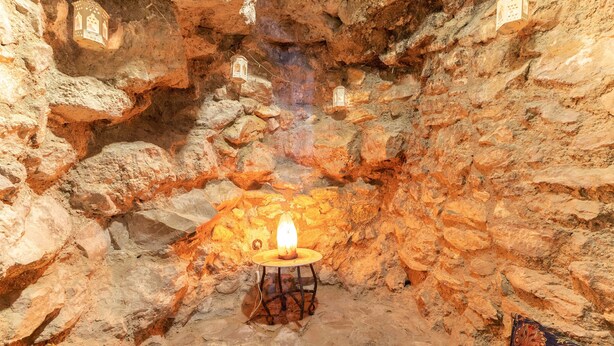 Interior de una cueva con una mesa central, faroles colgantes y una alfombra estampada.