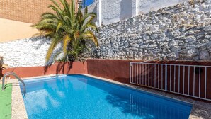 Una piscina con una pared de piedra y una palmera al fondo.