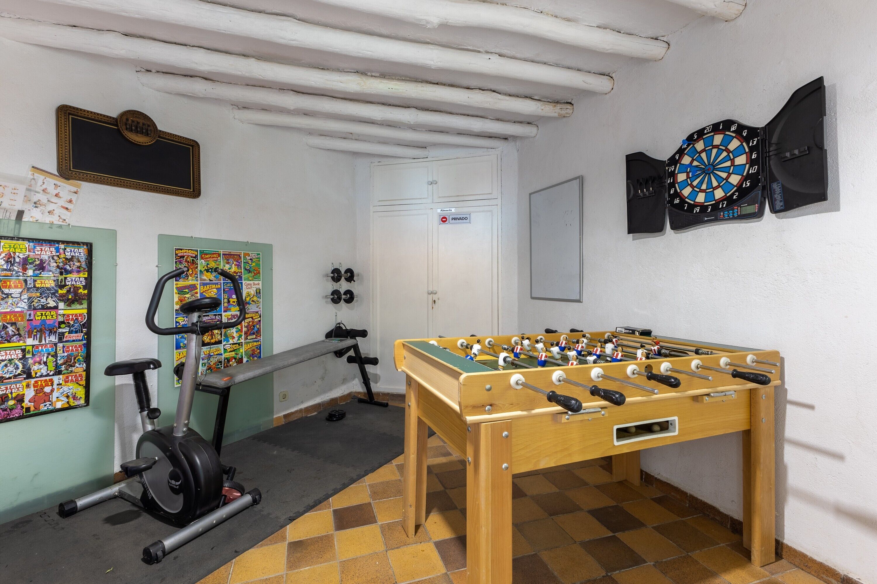 Ett rum med ett fotbollsspel, en motionscykel, en darttavla och en dörr med en skylt som visar ordet ”PIRAMIDO”.