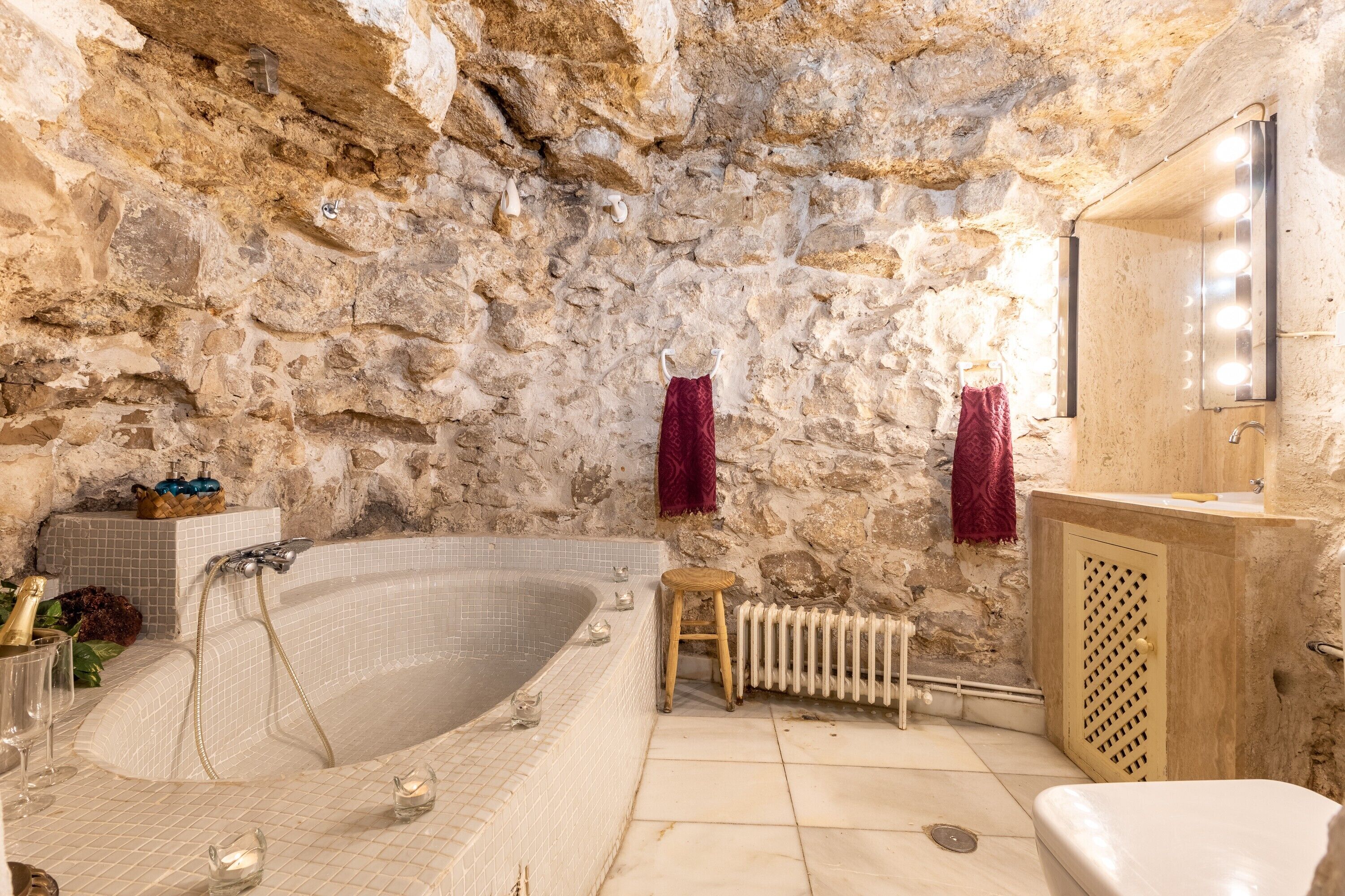 Un baño con paredes de piedra, una bañera, un tocador con espejo y un radiador.