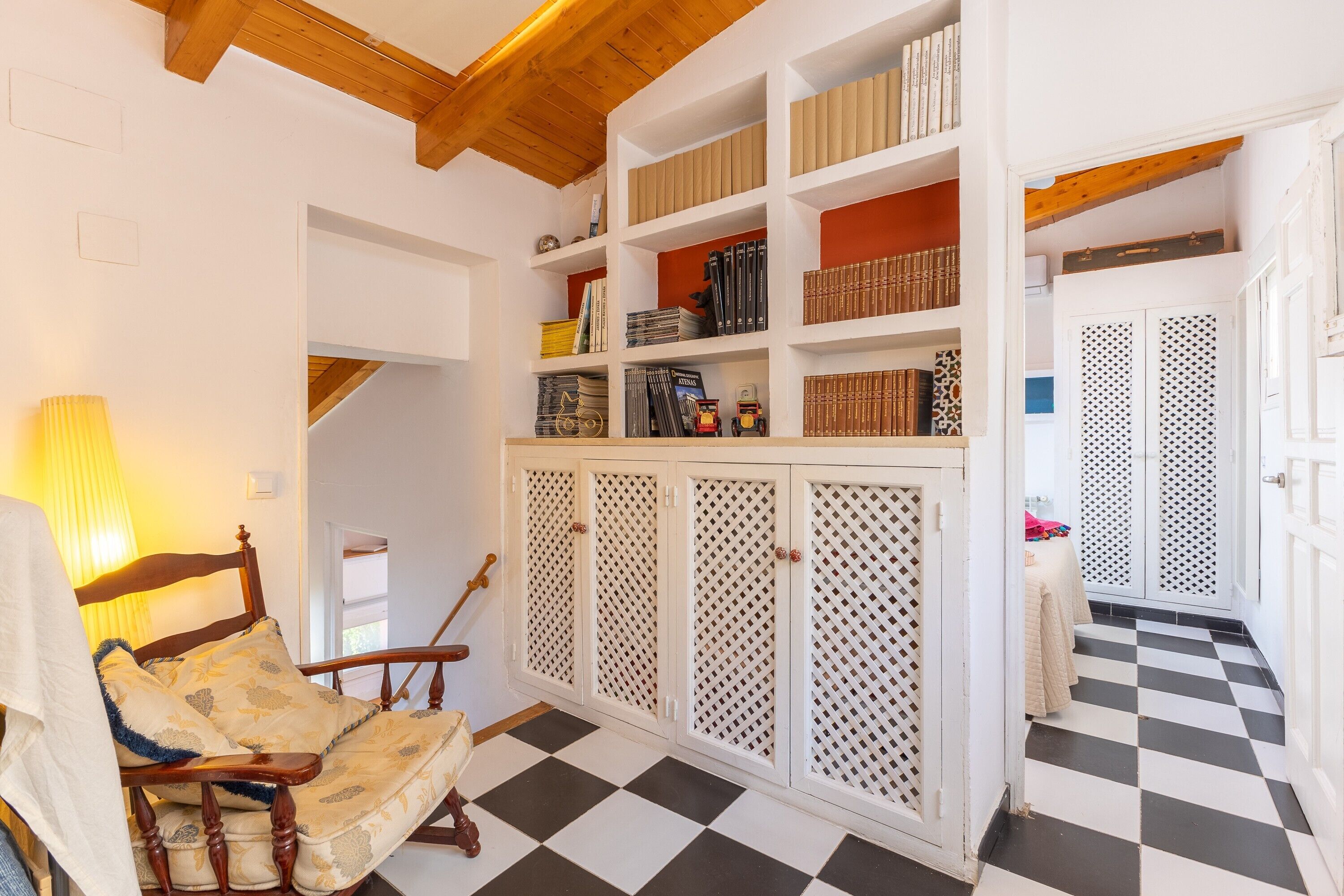 A room with a checkered floor, a wooden chair, a bookshelf, and a patterned door.
