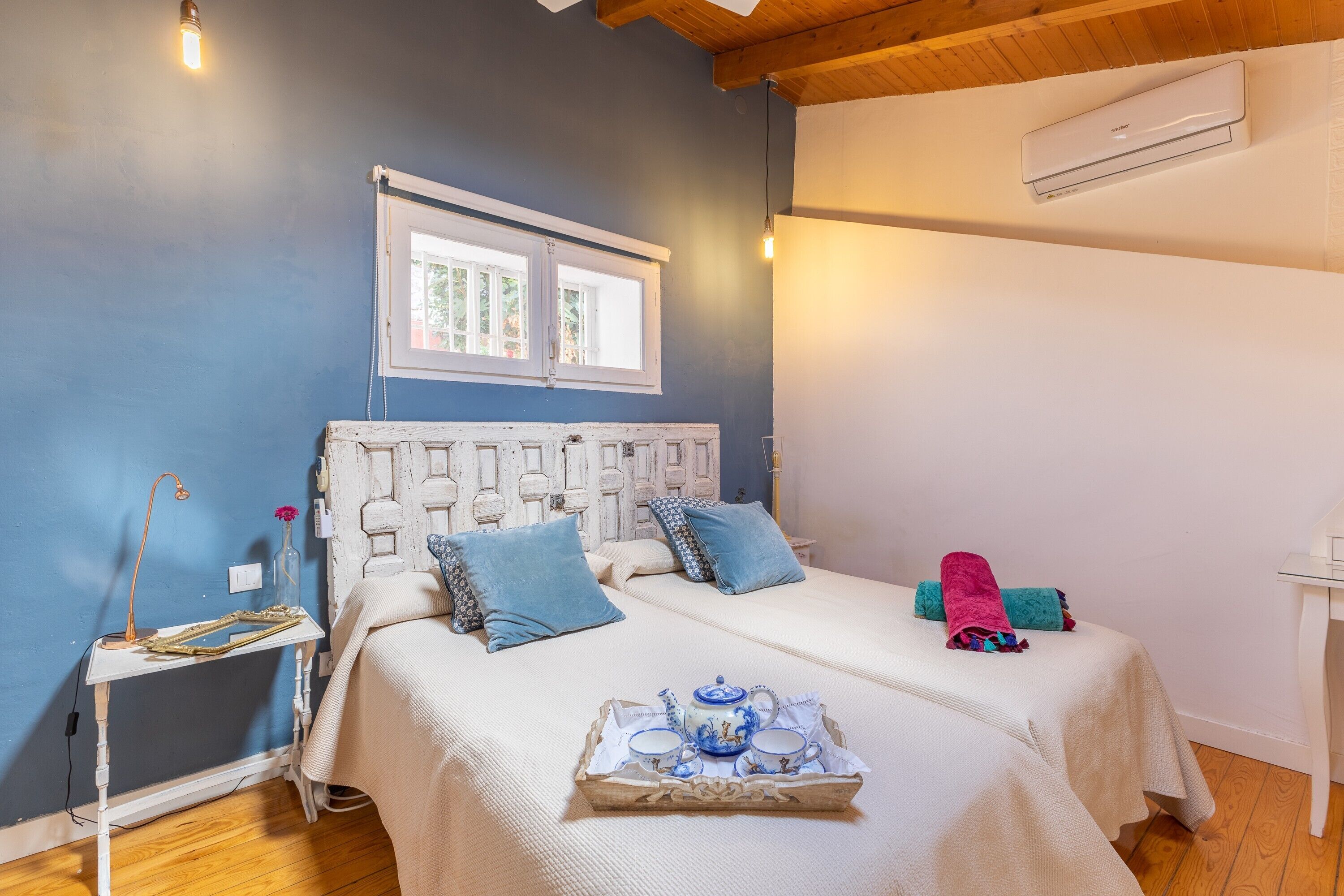 A bedroom with a bed, bedside table, window, and an air conditioning unit.