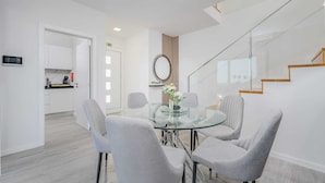 A modern dining area with a glass table and grey upholstered chairs, a kitchen in the background, and a staircase with wooden steps. - Where Serenity Meets Blue Horizons.  (Câmara de Lobos)
