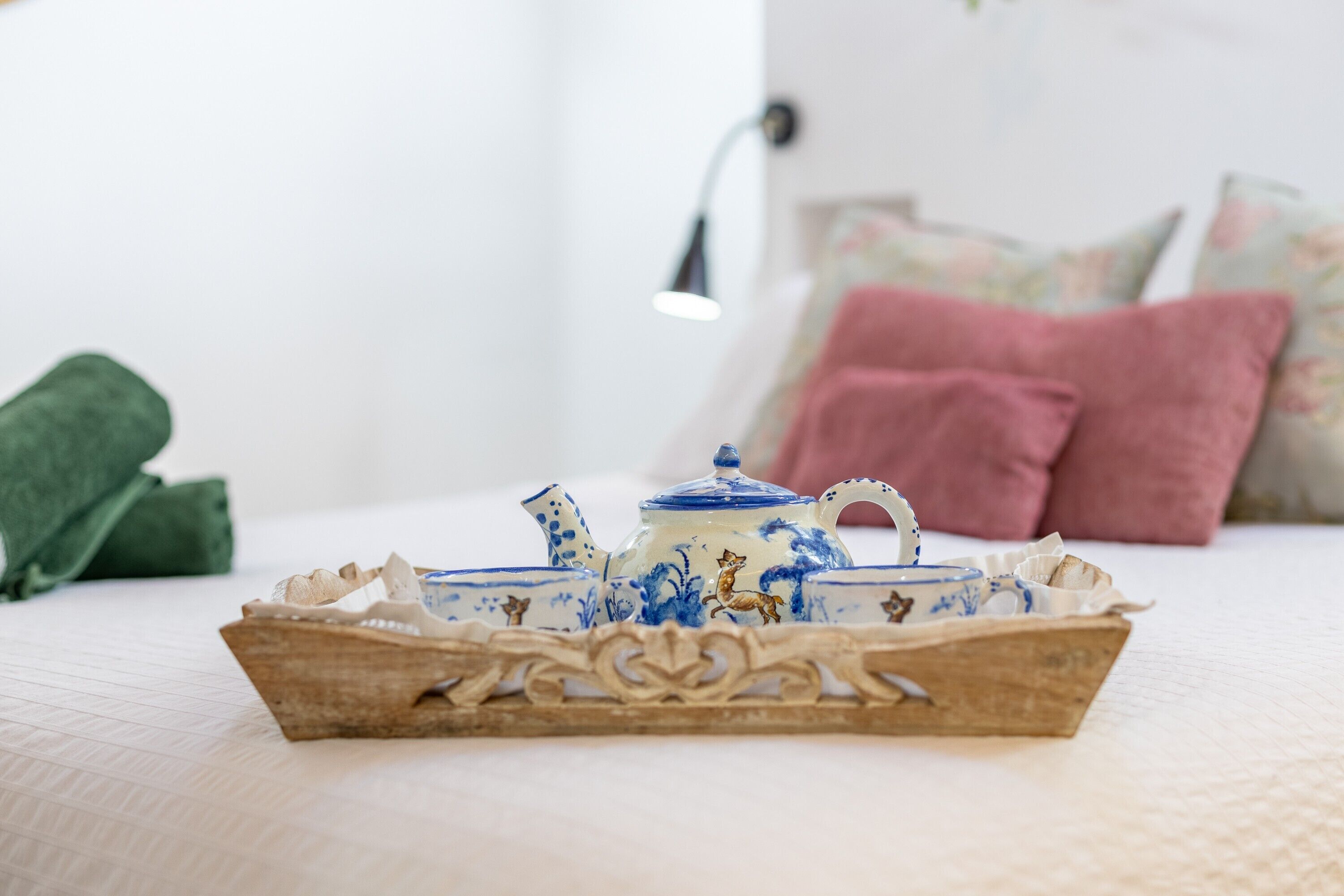 Ein Bett mit weißer Bettdecke, ein Holztischchen mit Teekanne und Tassen, und Kissen im Hintergrund.