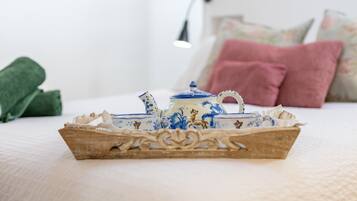 Ein Bett mit weißer Bettdecke, ein Holztischchen mit Teekanne und Tassen, und Kissen im Hintergrund.