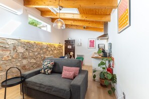 Un salon chaleureux avec un mur en pierre, un canapé gris, un luminaire suspendu et un plafond en bois.