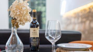 Una mesa con un jarrón de vidrio transparente con flores blancas, una botella de vino y una copa de vino vacía.