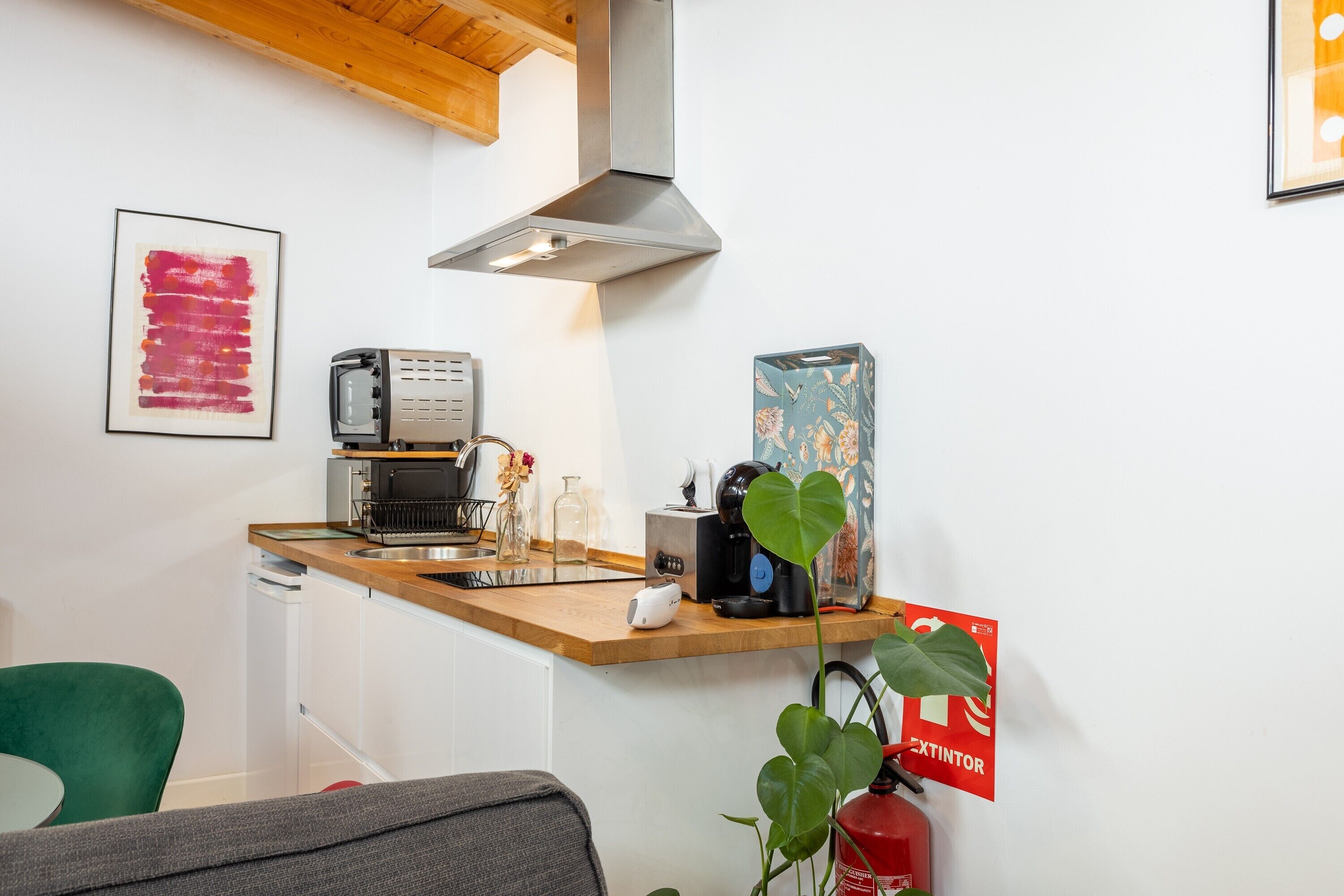 Una kitchenette con cafetera, tostadora y microondas. Hay un extintor de incendios montado en la pared y una planta en la esquina.