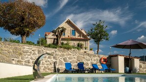 Una villa de piedra con piscina, sillas de descanso azules y un flotador.