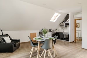 Eine moderne Küche mit Oberlicht, Essbereich mit Tisch für vier Personen und ein schwarzes Ledersofa.