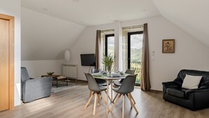 Una sala moderna con comedor, un sofá de cuero negro y un televisor.