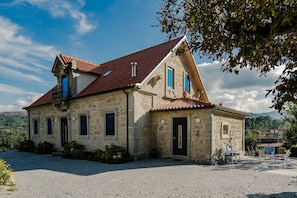A stone building with a red-tiled roof, a small balcony, and a door with a window.