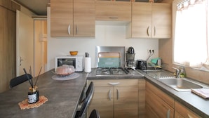 A compact kitchen with wooden cabinets, a gas stove, a microwave, and a sink. - Fully Equipped Chalet V Near the Sea with Shared Pool, Private Terrace, and Air Conditioning (Pianottoli-Caldarello)
