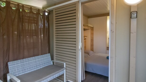 A room with a bed, a bench, and a sliding door leading to another room. - Fully Equipped Chalet V Near the Sea with Shared Pool, Private Terrace, and Air Conditioning (Pianottoli-Caldarello)