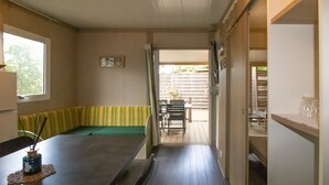 A room with a dining table, chairs, a bench, a window, and a door leading to an outdoor area. - Fully Equipped Chalet V Near the Sea with Shared Pool, Private Terrace, and Air Conditioning (Pianottoli-Caldarello)