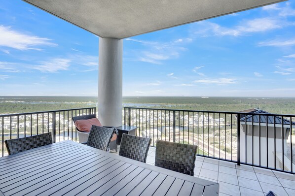 A balcony with a view of a distant landscape, a table, and wicker chairs.