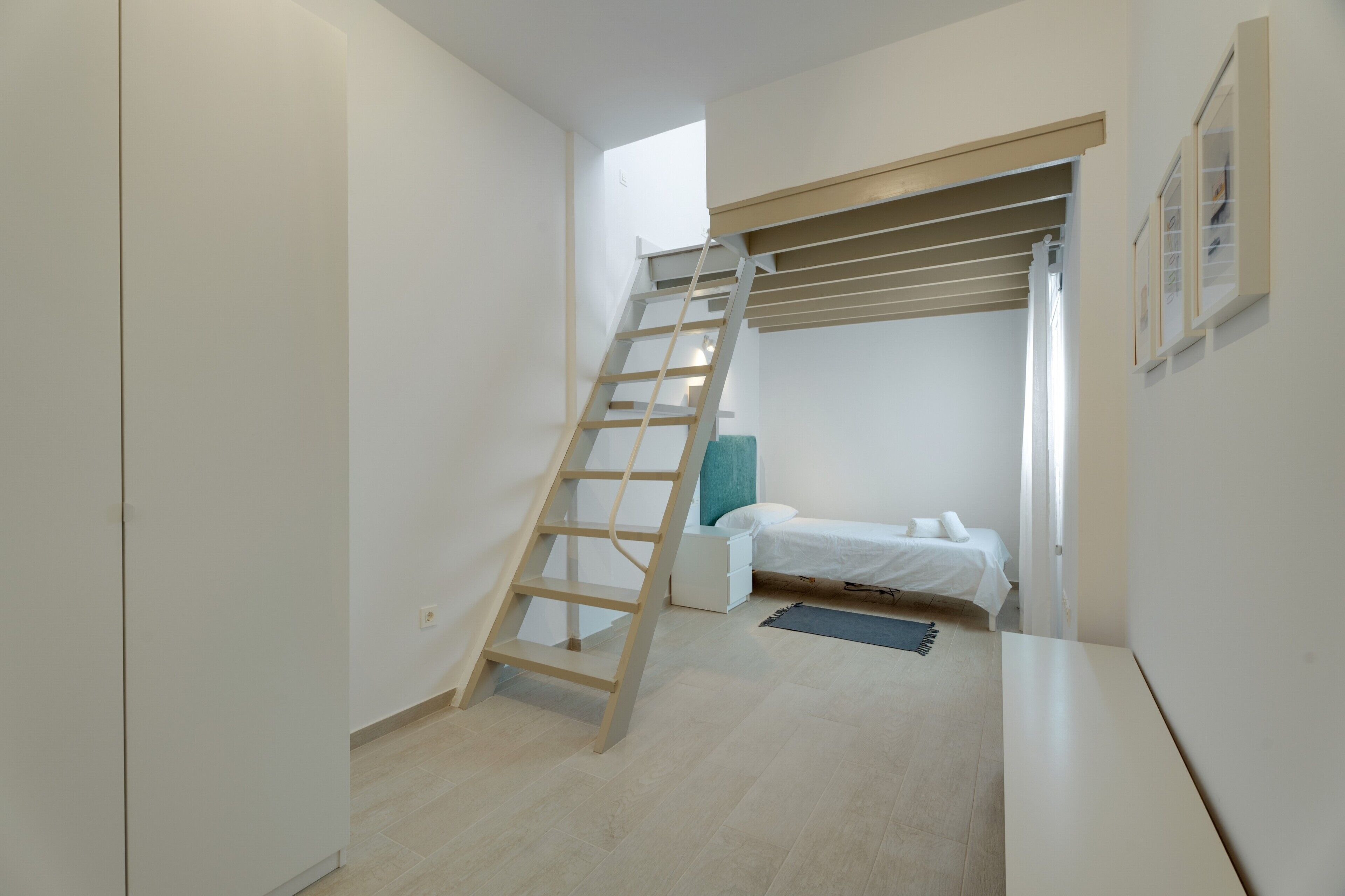 Une chambre avec une échelle en bois, un lit, un petit bureau et une fenêtre.