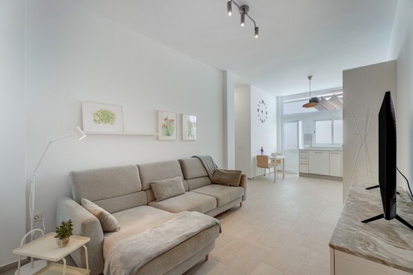 Ein modernes Wohnzimmer mit einer Couch, einem kleinen Tisch mit Pflanze, einem Flachbildfernseher und Kunstwerken an der Wand.