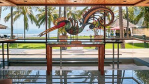 A modern interior with a large glass window overlooking a pool and palm trees, featuring a unique metal sculpture.