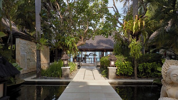 A pathway leading to a building surrounded by lush greenery and a body of water.