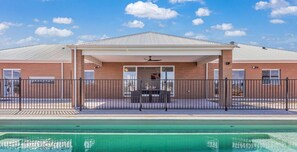 A building with a covered patio area, a pool, and a fenced outdoor space.