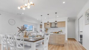 Una cocina moderna con armarios blancos, iluminación colgante y un comedor con sillas blancas.