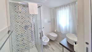 Un baño moderno con ducha de vidrio, inodoro, bidé y lavabo con espejo.