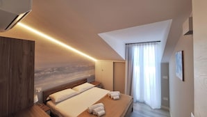 Una habitación de hotel moderna con una cama grande, una mesita de noche de madera y un acondicionador de aire instalado en el techo.