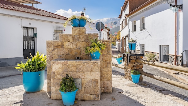 A stone fountain with potted plants, a street with buildings, and a clear sky. - Apartment 'Postero' with Mountain View, Balcony and Wi-Fi (Jérez del Maquesado)