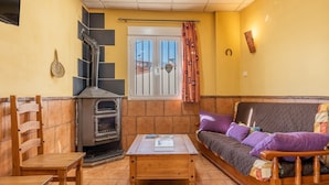 A living room with a sofa, a wooden table, a fireplace, and a window with curtains. - Apartment 'Postero' with Mountain View, Balcony and Wi-Fi (Jérez del Maquesado)