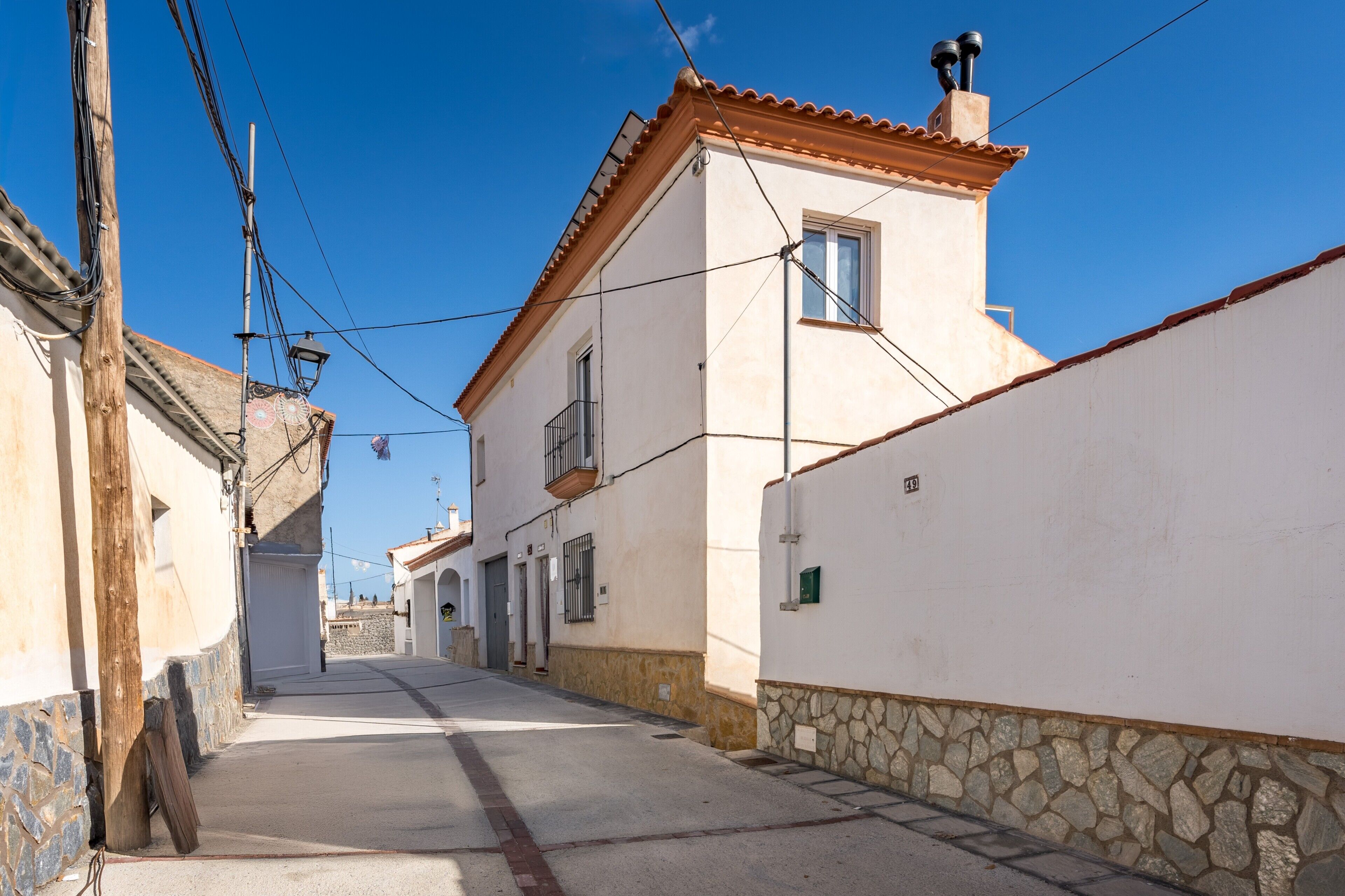 Une rue étroite, bordée de bâtiments des deux côtés, un ciel bleu dégagé et un lampadaire bien visible.