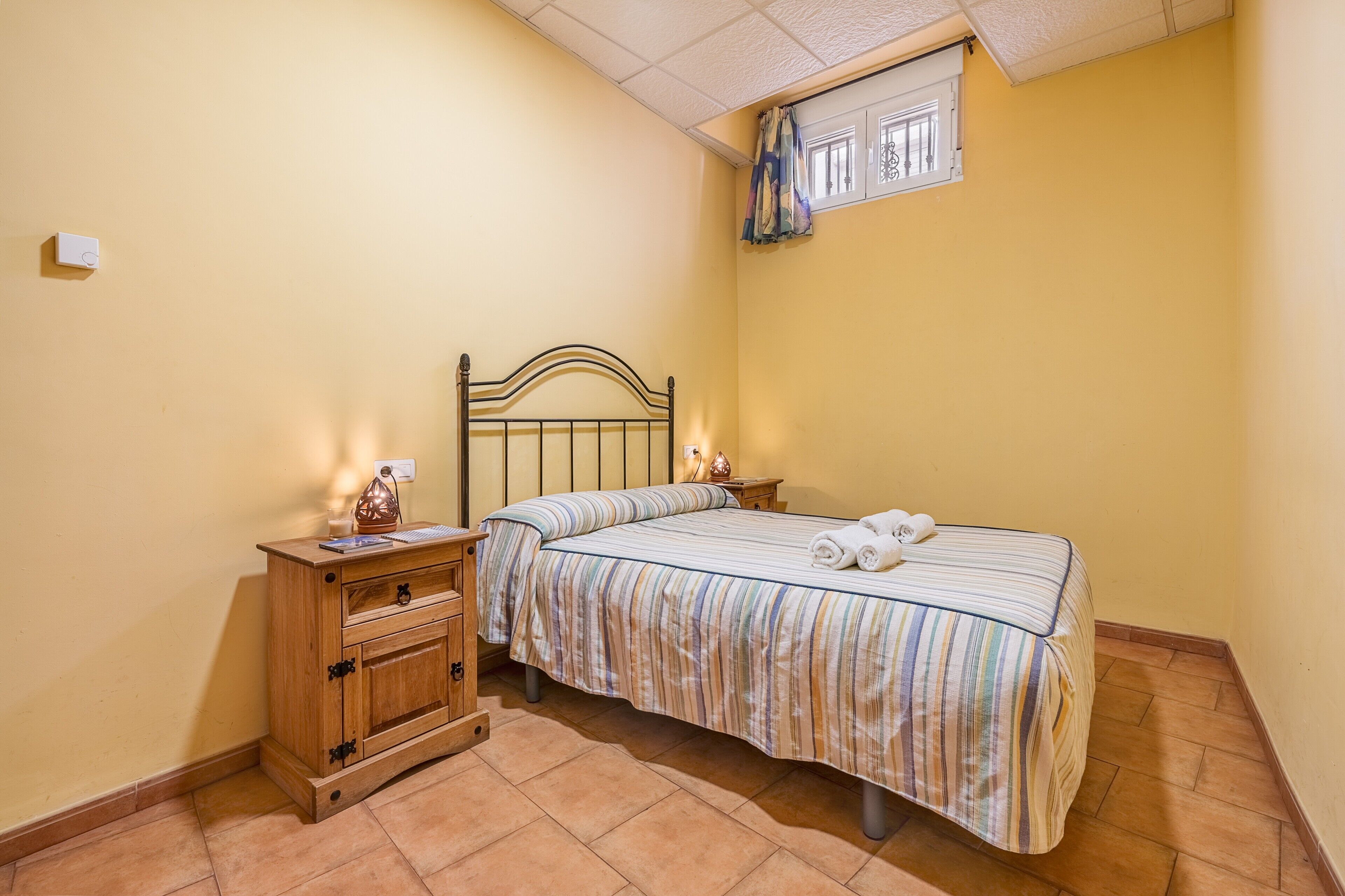 Un dormitorio con cama, mesitas de noche, cómoda de madera y una ventana con cortinas.