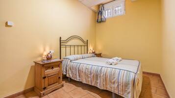Un dormitorio con cama, mesitas de noche, cómoda de madera y una ventana con cortinas.