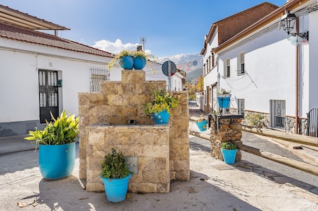 Een stenen fontein met potplanten, een straatbeeld met gebouwen en een heldere lucht.. Apartment 'Tizná' with Mountain View, Shared Terrace and Wi-Fi