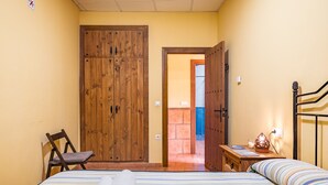 A bedroom with a bed, a chair, a wooden wardrobe, and a nightstand with a lamp. - Apartment 'Tizná' with Mountain View, Shared Terrace and Wi-Fi (Jérez del Maquesado)