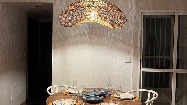 Een eetgedeelte met een ronde tafel voor vier personen, omringd door witte stoelen, onder een bijzondere plafondlamp.