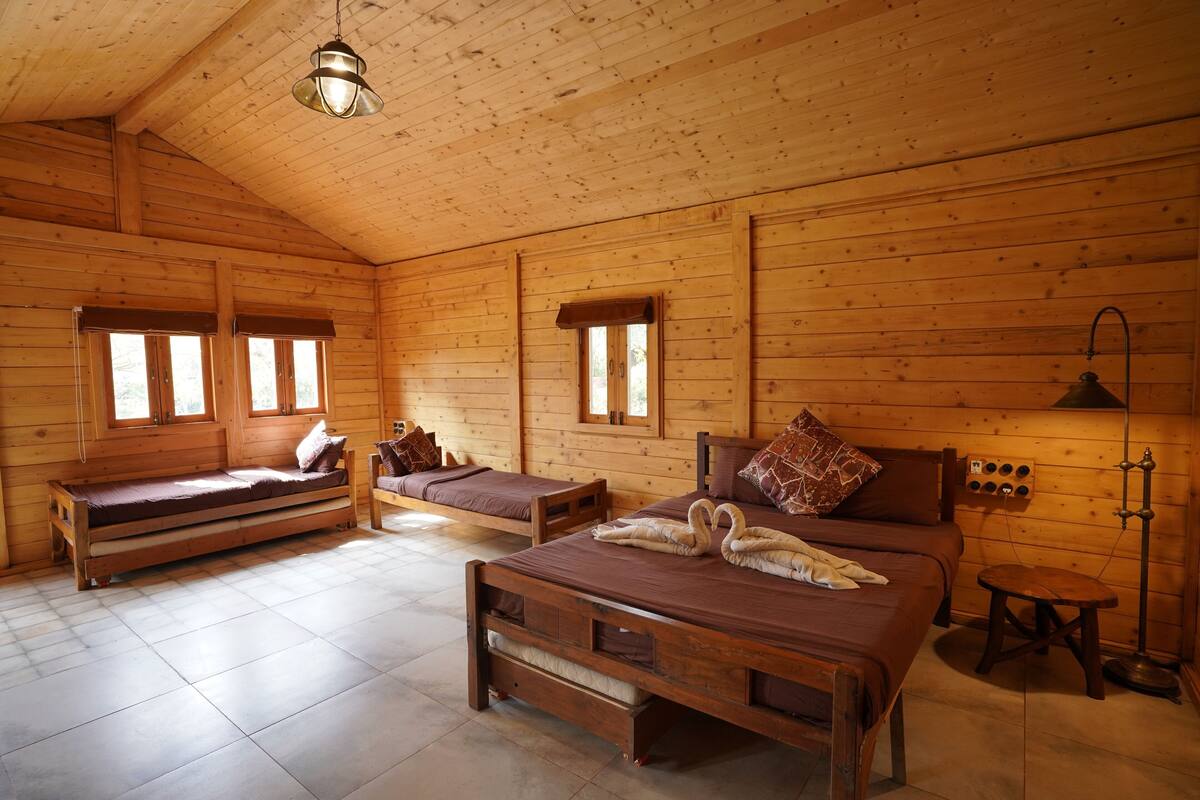 Quarto de cabana de madeira com duas camas, um banco e uma pequena mesa.